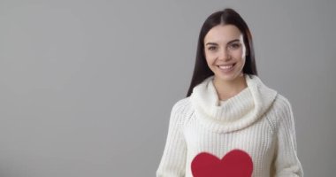 Gri arka planda kırmızı kağıt kalpli güzel bir genç kadın.