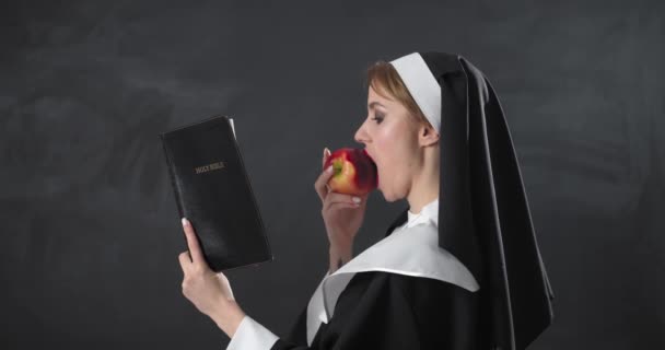 Sexy Nonne Liest Bibel Und Isst Apfel Auf Dunklem Hintergrund — Stockvideo