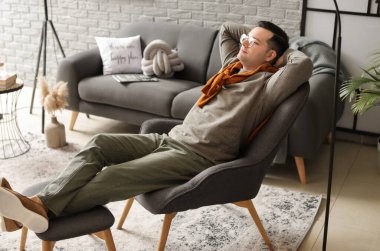 Evdeki koltukta dinlenen genç adam.