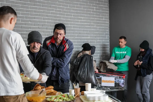 Volunteers giving food and clothes to homeless people in warming center