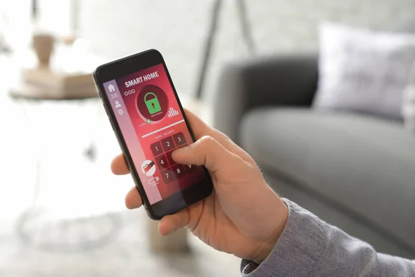 Man with mobile phone using smart home security system application, closeup