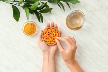 Hafif arka planda zerdeçal hapları olan kadın elleri