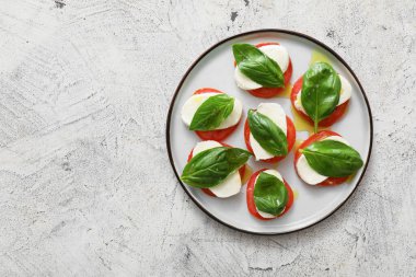 Mozarella peynirli, domatesli ve arkaplanda fesleğenli tabak.