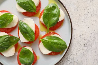 Mozarella peynirli, domatesli ve arkaplanda fesleğenli tabak.