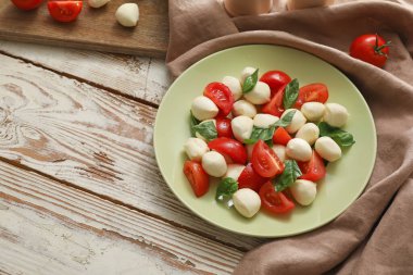 Ahşap arka planda mozarella peyniri, domates ve fesleğen tabağı.