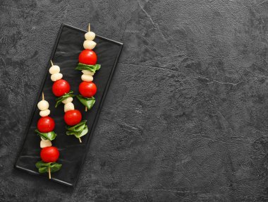 Koyu arkaplanda mozarella peyniri, domates ve fesleğen çubukları.