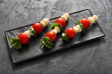 Koyu arkaplanda mozarella peyniri, domates ve fesleğen çubukları.