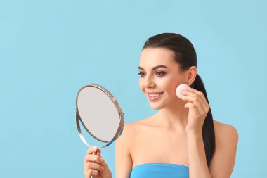 Makyaj süngeri ve arka planda ayna olan güzel bir genç kadın.