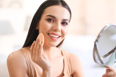 Güzel genç bir kadın evde makyaj yapıyor.