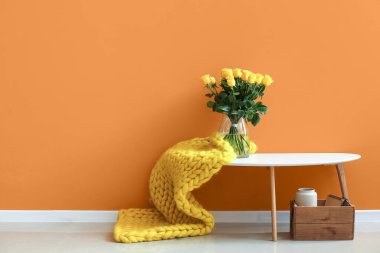 Odanın duvarının yanındaki masanın üzerinde güzel sarı güller olan vazo.