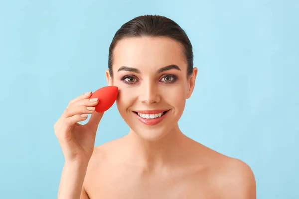 Beautiful young woman with makeup sponge on color background