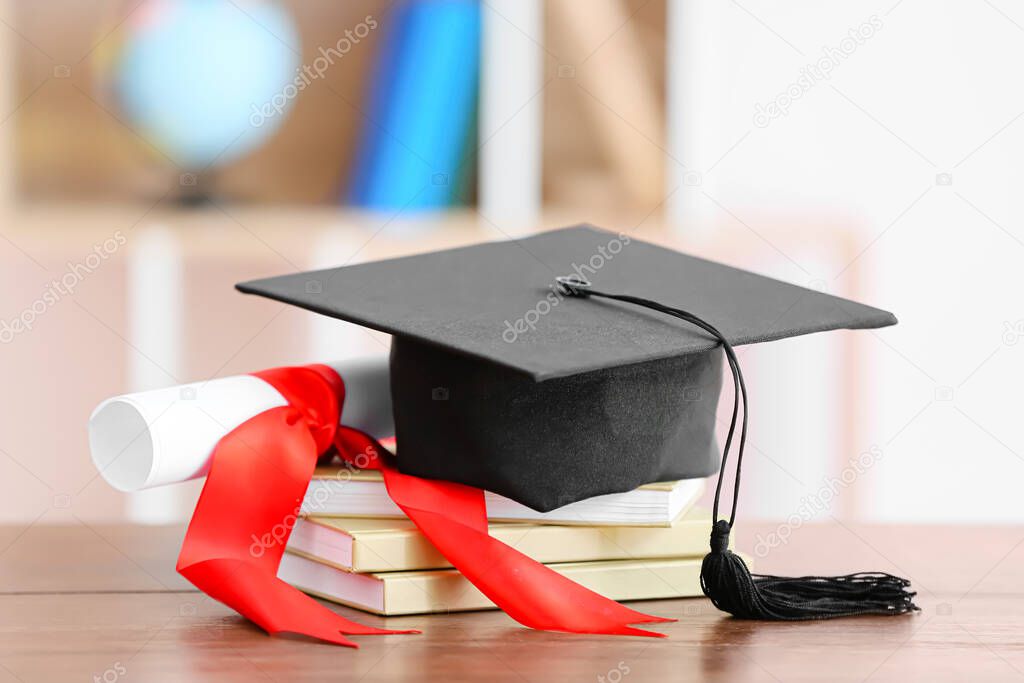Graduation hat with diploma and books on table indoors