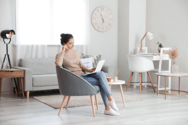 Evdeki koltukta dizüstü bilgisayarlı güzel bir kadın oturuyor.