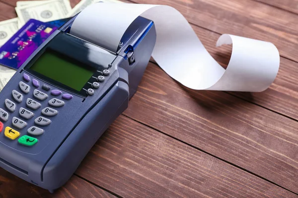 Payment terminal with credit cards and money on wooden background, closeup