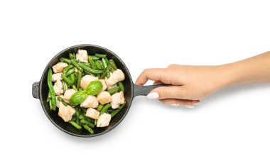 Elinde tavayla lezzetli yeşil fasulye ve beyaz arka planda tavuk tutan bir kadın.