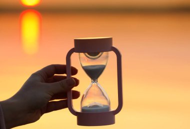 Gün batımında nehrin yanında şık kum saati olan bir kadın.