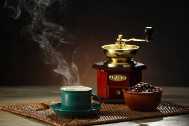 Tahta arka planda bir fincan sıcak kahve ve öğütücü.