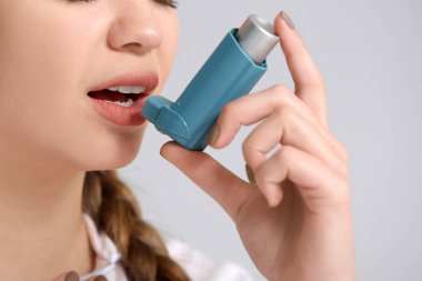 Astımı olan genç bir kadın gri arka planda astım krizi geçiriyor. Yakın plan.