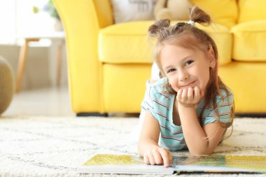 Evde kitap okuyan sevimli küçük bir kız.