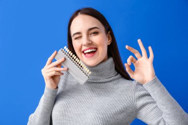 Diş rengi çizelgesi olan genç bir kadın mavi arka planda iyi görünüyor.