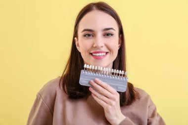 Sarı arka planda diş rengi çizelgesi olan genç bir kadın.