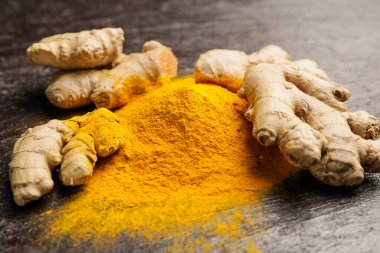 Siyah arkaplanda zerdeçal tozu ve kökleri