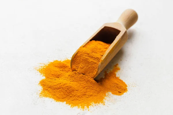 Scoop with turmeric powder on light background