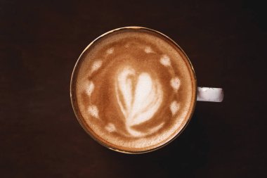 Ahşap arka planda latte sanatıyla bir fincan kahve.