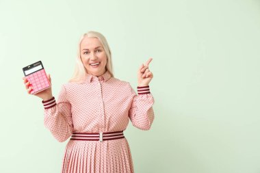 Hesap makinesi olan olgun bir kadın renk arkaplanını işaret ediyor