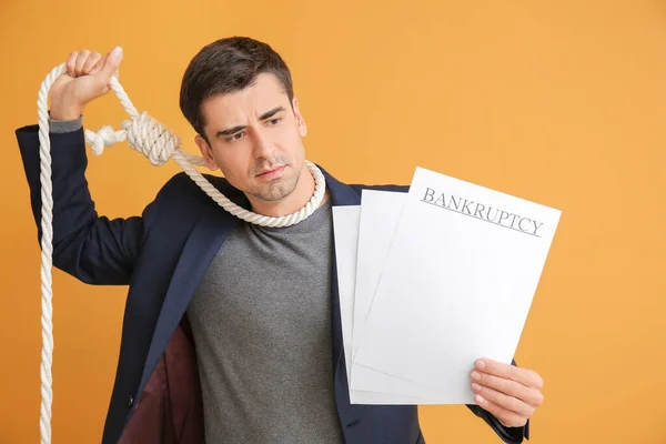 Stressed man with rope on neck and documents on color background. Bankruptcy concept
