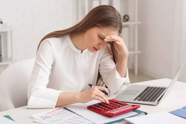 Stressed female accountant with calculator working in office