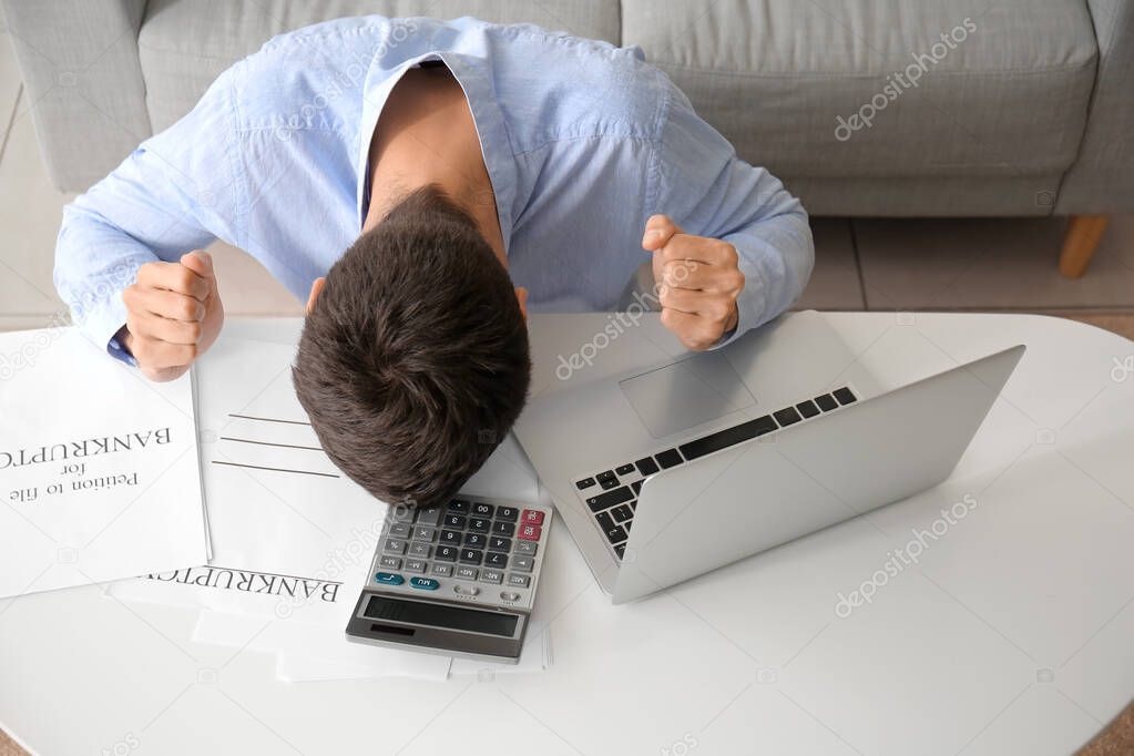 Stressed man with laptop and calculator at home. Bankruptcy concept