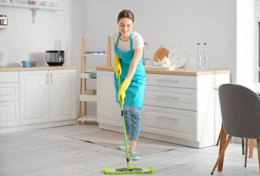 Mutfakta yerleri paspaslayan genç kadın.