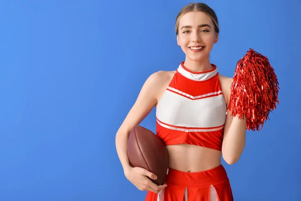 Beautiful young cheerleader with ball on color background