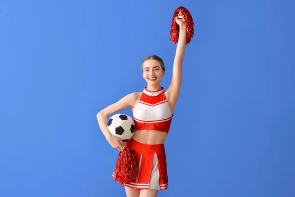 Beautiful young cheerleader with ball on color background