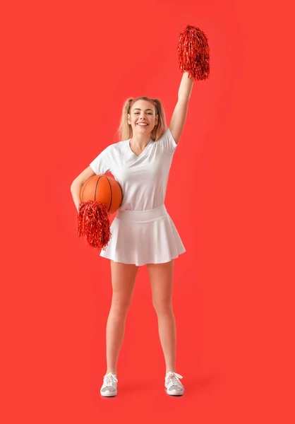 Beautiful young cheerleader with ball on color background