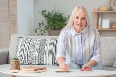 Hesap makinesiyle evde bütçesini planlayan olgun bir kadın.