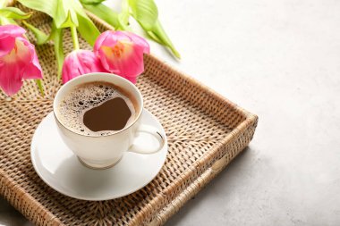 Hafif arka planda bir fincan kahve ve çiçekli tepsi.