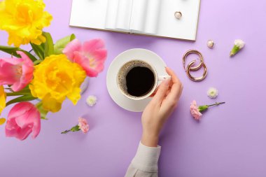 Bir fincan kahve ve arka planda bahar çiçekleri olan bir kadın eli.