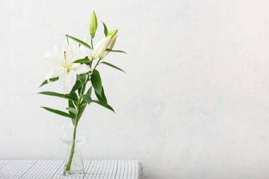 Masada açık arkaplanda güzel zambak çiçekleri olan vazo.