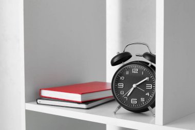 Kitapları ve çalar saati olan modern raf ünitesi, yakın plan.