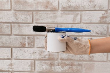 Tuğla arka planda boya ve fırçayla bir kadın eli