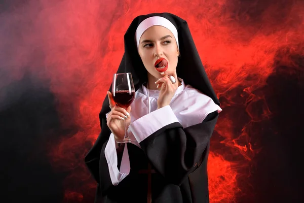 Naughty nun with glass of wine on dark background