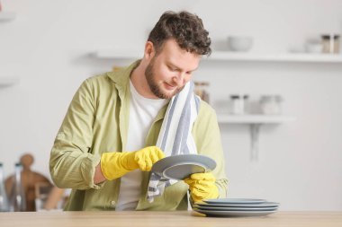 Genç adam mutfakta masaları siliyor.