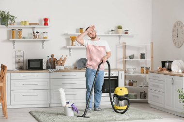 Genç adam mutfakta halı süpürüyor.