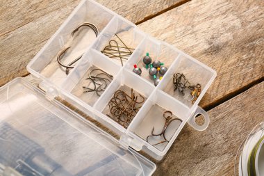 Ahşap zemin üzerinde farklı balıkçılık ekipmanları olan plastik kutu.