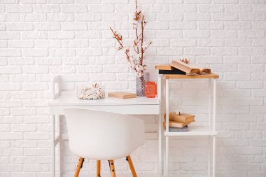 Hafif tuğla duvarın yanında eski kitaplar ve pamuk çiçekli bir masa.