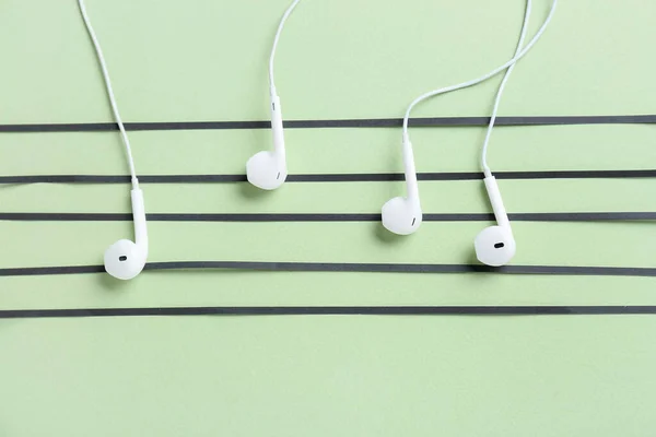 Music notes made of modern earphones on color background