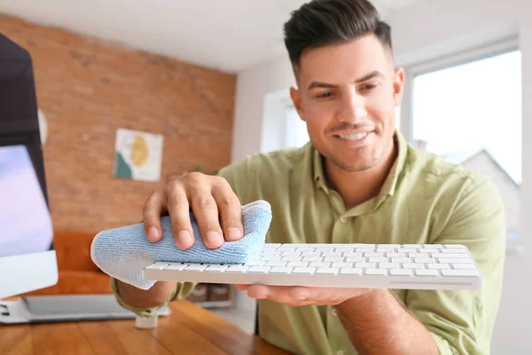 Young man cleaning PC keyboard at home