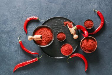 Koyu arkaplanda kırmızı biber tozu olan kâseler ve kepçeler